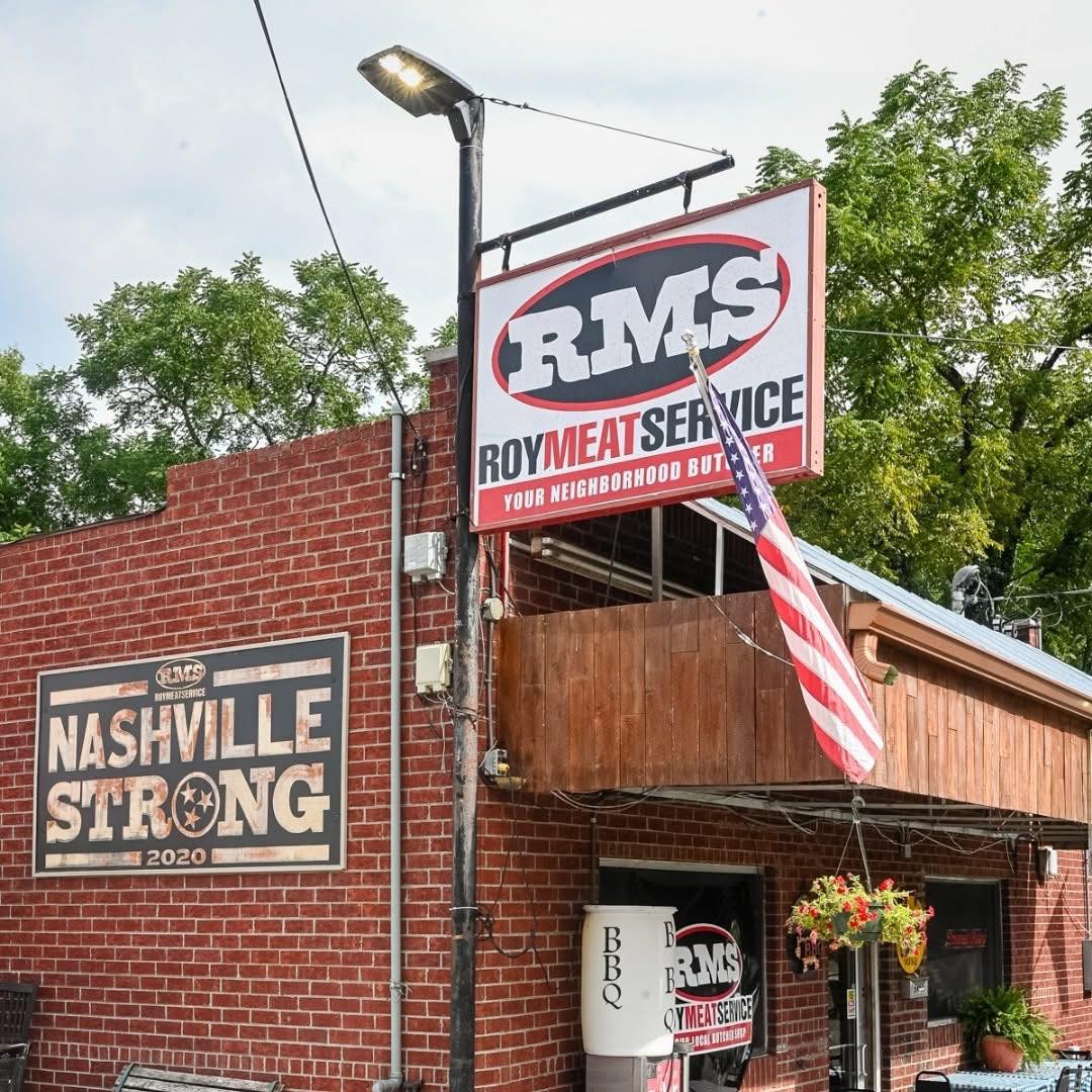 Roy Meat Service storefront. Brick building with RMS sign, Nashville Strong 2020 painted on the side, American flag hanging from the awning. East Nashville.