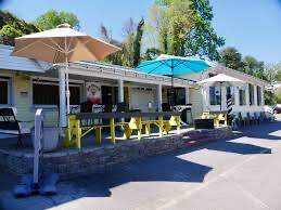 The patio at Lake Hickory Pub and Marina, teal umbrellas and a yellow-topped rail, tables set at the water's edge