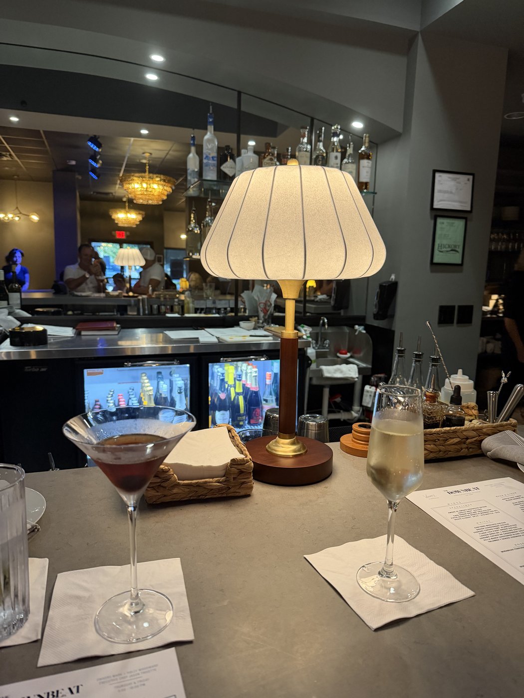 The dim, warm-lit bar at The Downbeat, a lamp and two cocktails on the counter