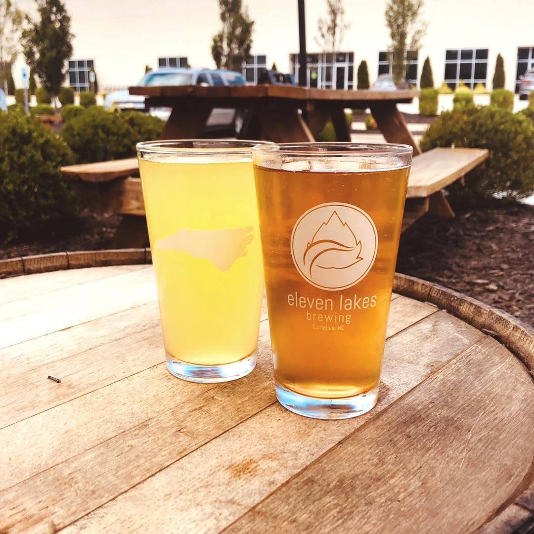 Two Eleven Lakes Brewing pints on a barrel table, the picnic-table patio behind